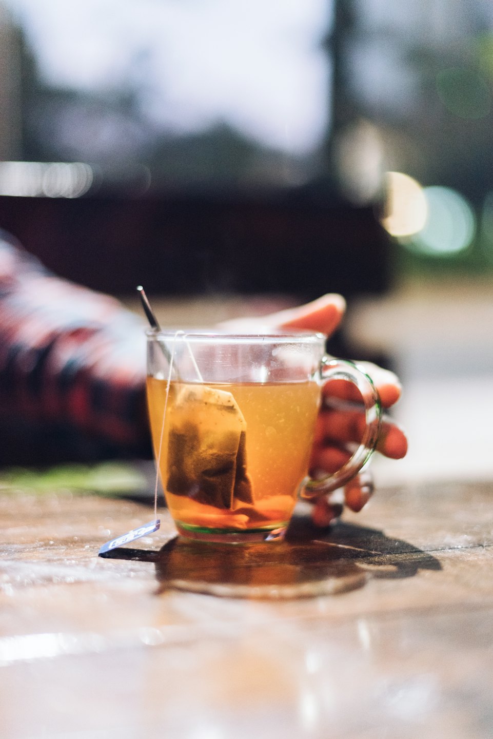 Hand holding a mug of tea with teabag on a wooden table.