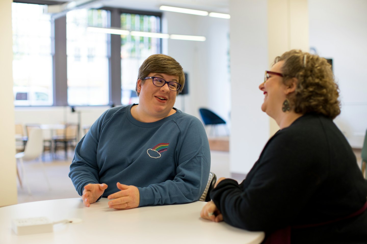 Two colleagues cheerfully discussing ideas at a modern office table.
